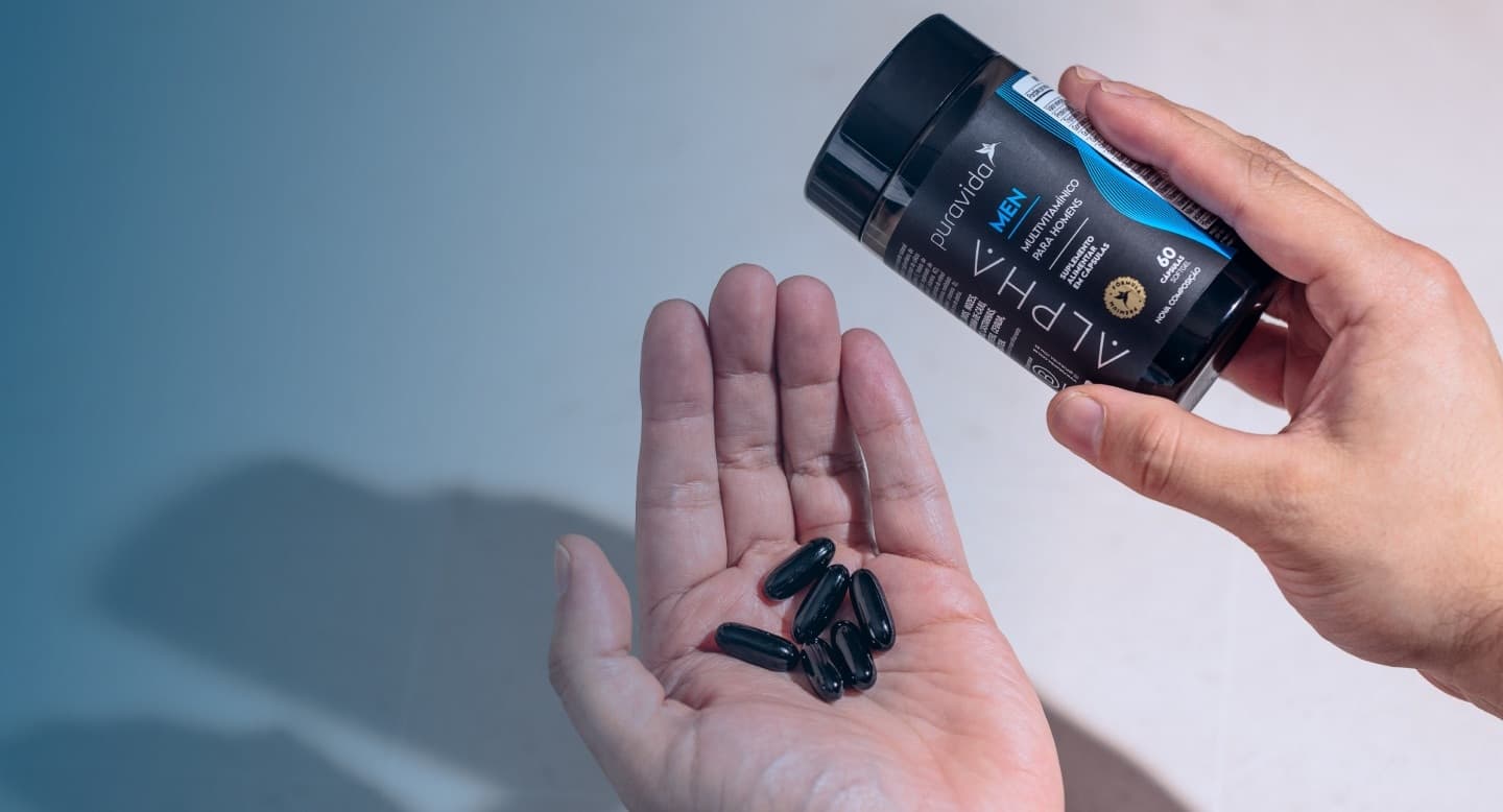 Mão segurando o frasco de Alpha Men com as cápsulas softgel