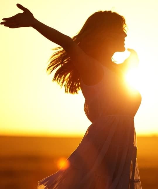 Mulher de braços abertos ao pôr do sol