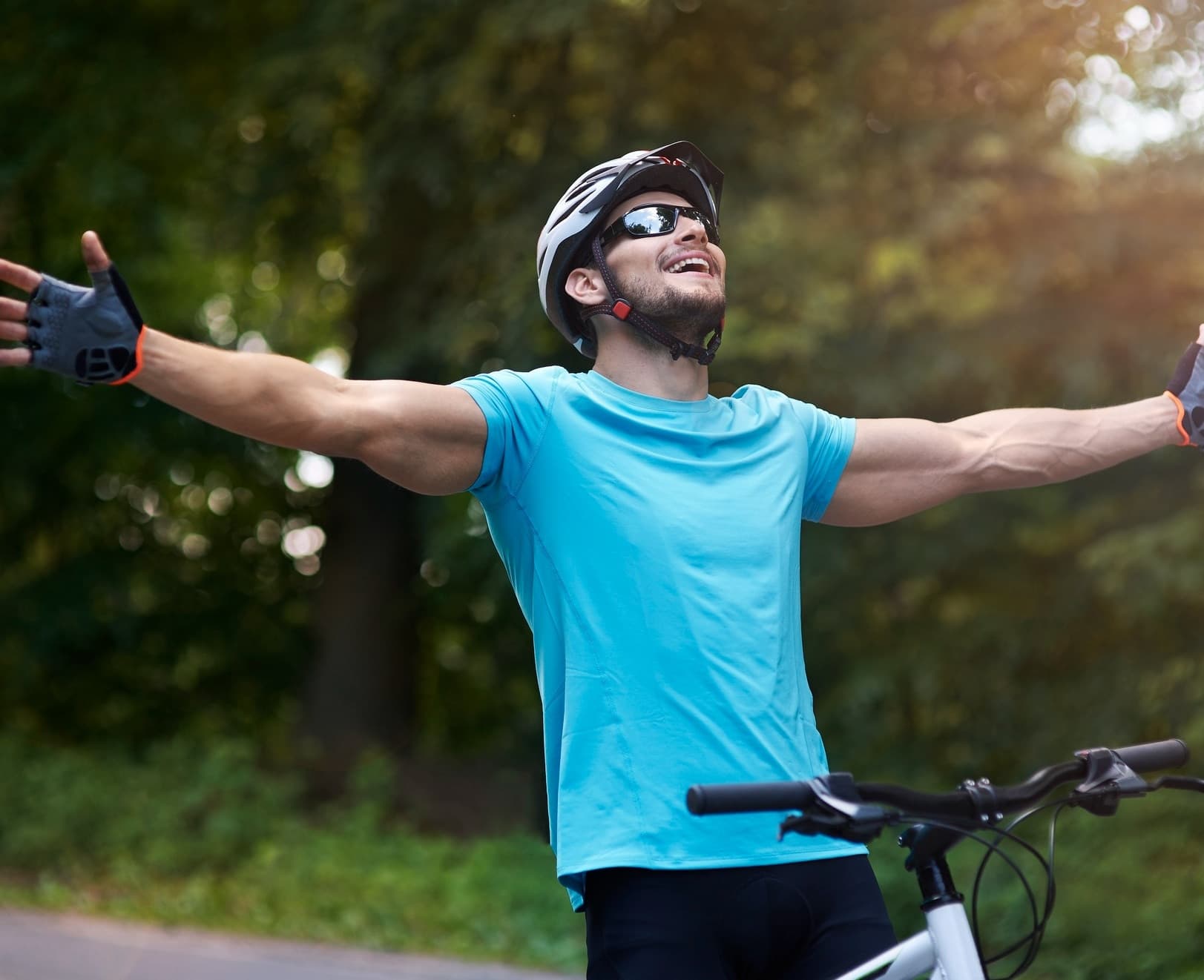 Homem de bicicleta com os braços abertos ao ar livre