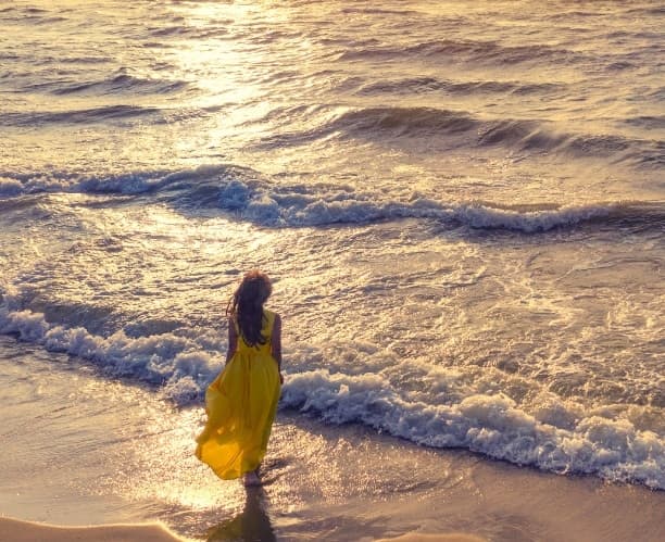 Mulher caminhando na praia ao pôr do sol